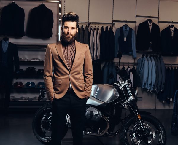 Fashionable man posing next to a retro sports motorbike at the men's clothing store.